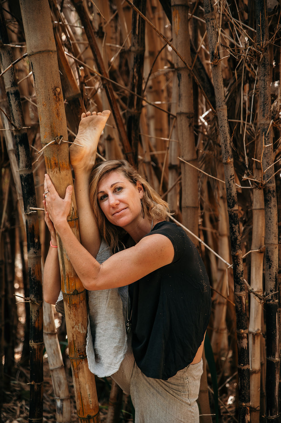 Nieke in a deep hamstring stretch with one leg propped on a tree trunk, practicing yoga in a peaceful natural environment