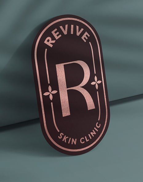 A rose gold foil sticker featuring the Revive Logo on a green background
