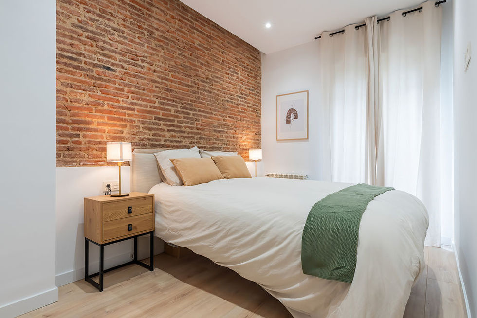 Habitación con cama doble, pared de ladrillo y cortinas blancas