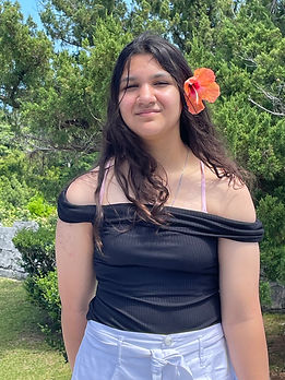 Picture of Alessandra D'Addona, our Treasurer. She is posing in front of foliage with a flower in her hair.