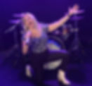 Raquel, lead vocalist of Raquel's Riot, passionately singing into a sparkling microphone while wearing stylish boots