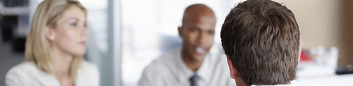This photograph shows a man in the foreground speaking to a businessman and woman.