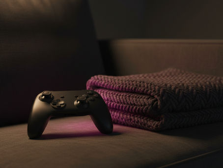 A black game controller set down on a dark couch cushion beside a folded magenta knit blanket in a dim living room.