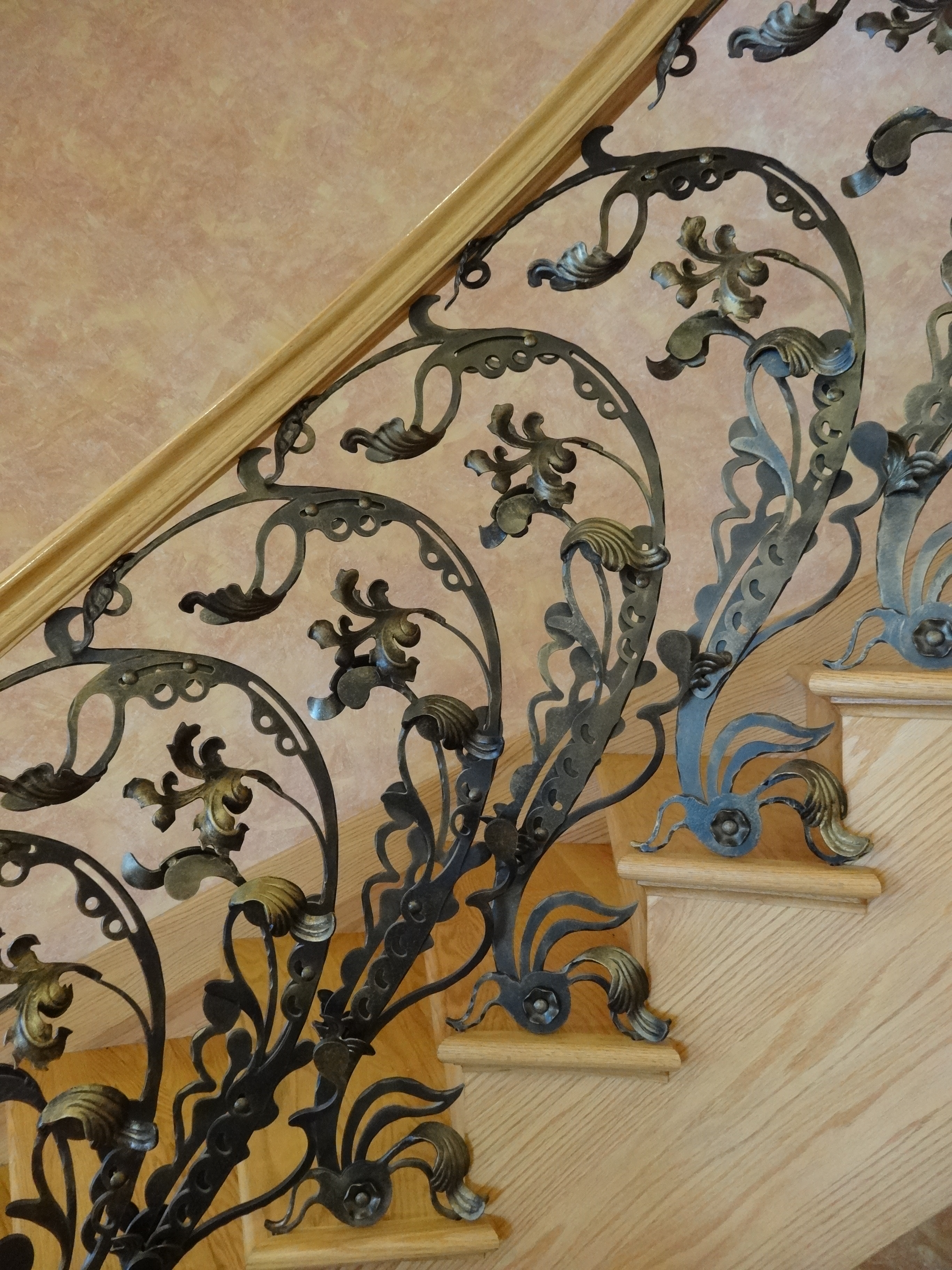 Ornate interior iron railing with cascading leaf motifs and a wood handrail.