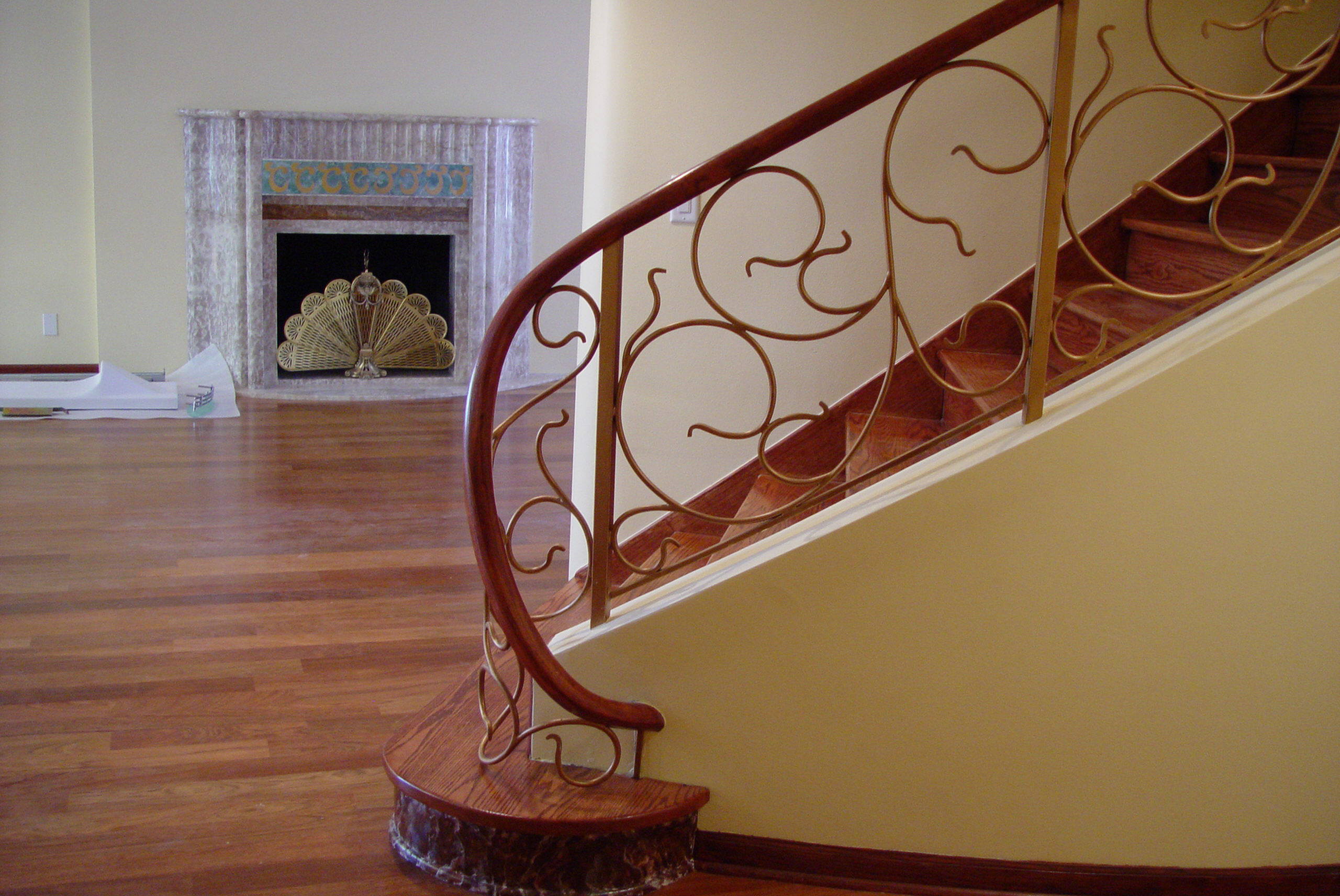 Curved interior metal railing with flowing scrollwork and a wood handrail.