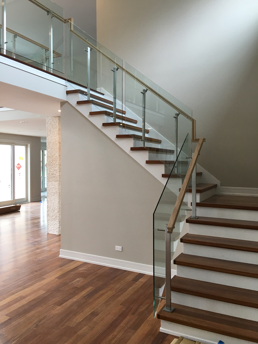Interior glass staircase railing with warm wood handrails and refined metal fittings.