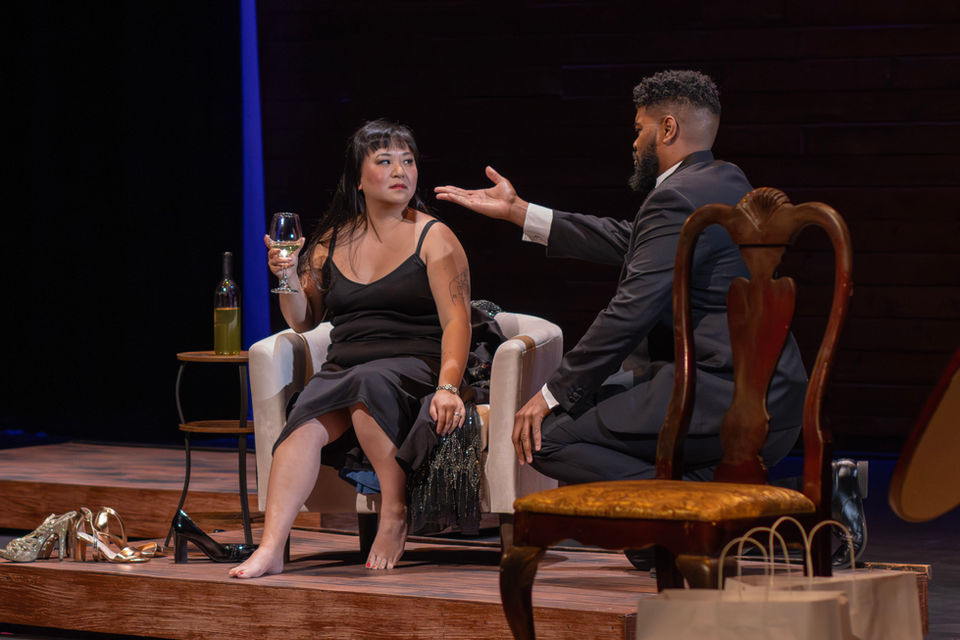 Man gesturing toward a woman sitting in an armchair on stage