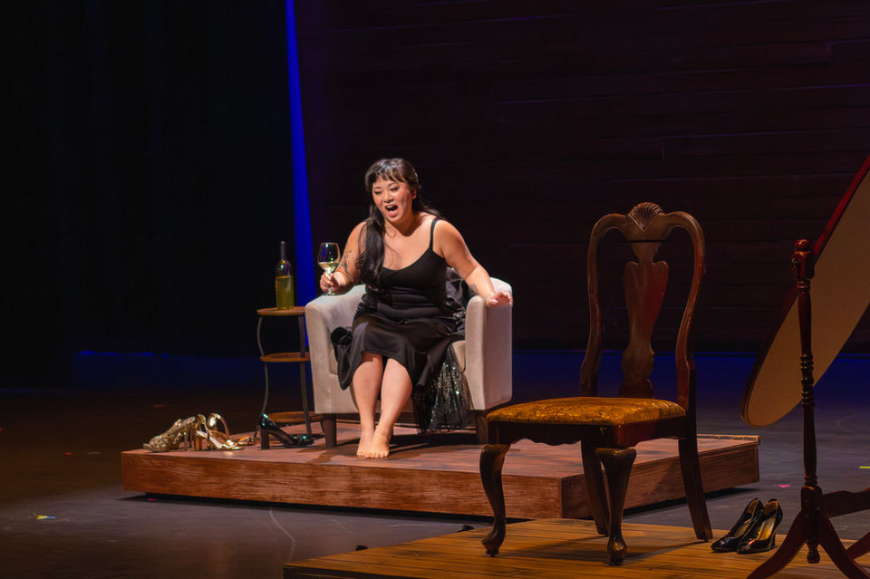 Woman in black dress performing on stage in an armchair