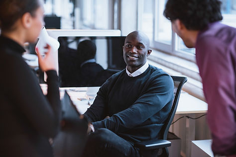 A smiling man sitting at his desk and turned around talking to his coworkers about his successful session with a life coach