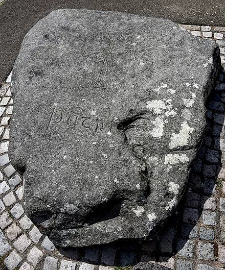 A photo of a large stone featuring a carved cross which is the reputed burial place of Saint Patrick in Downpatrick