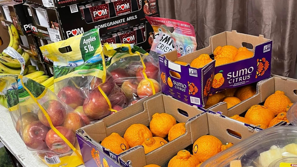 A close-up image of the fruit section of the Second Harvest Shop Through in our Nutrition Room. Pictures are apples, oranges, pomegranates, and bananas.