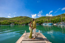 Smiling couple holding hands on a dock in Marigot Bay, St. Lucia, surrounded by lush green hills and