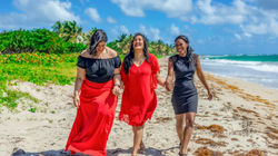 Three women laughing and walking hand-in-hand along Anse Des Sables, a tropical beach in St. Lucia d