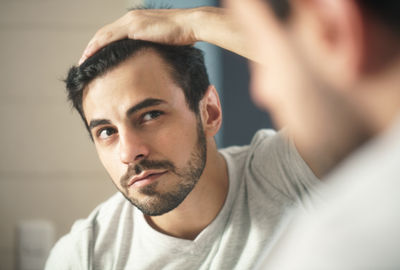 Man looking in the mirror, pleased with the results of his PRP hair restoration treatment in NYC.