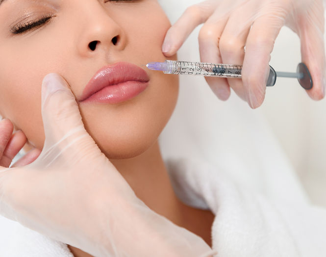 Hand holding a syringe next to a beautiful face, preparing for a lip injection.