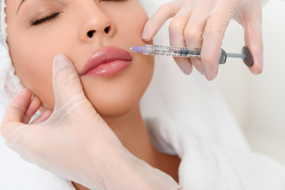 Hand holding a syringe next to a beautiful face, preparing for a lip injection.
