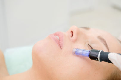 A woman undergoing a microneedling procedure on her face with a specialized device to create tiny punctures in the skin in NYC.