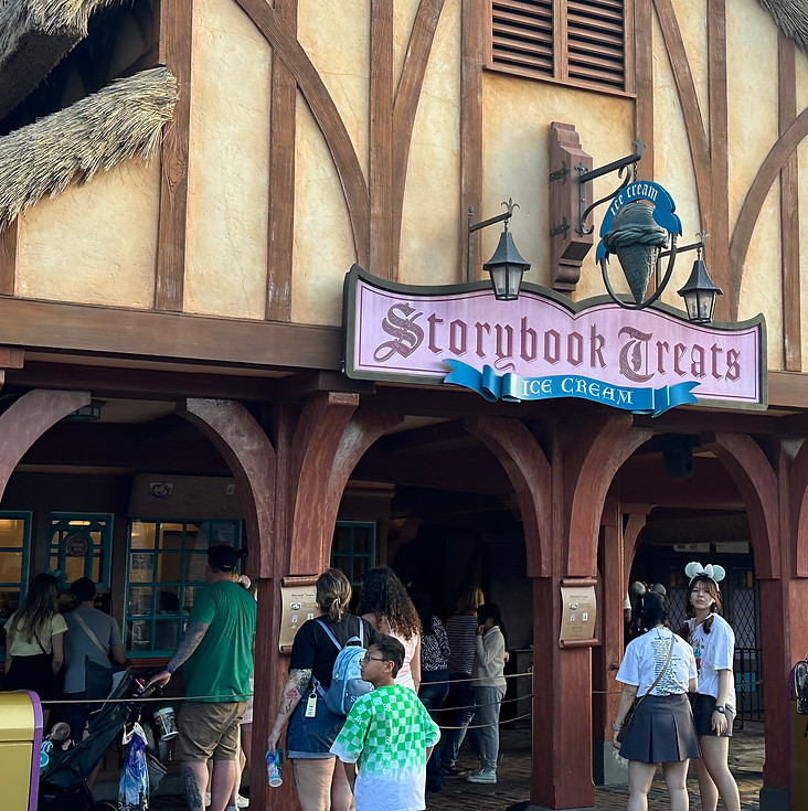Storybook Treats in Fantasyland, with a cottage-style exterior, soft blue trim, and a quaint sign inviting guests to enjoy sweet treats.