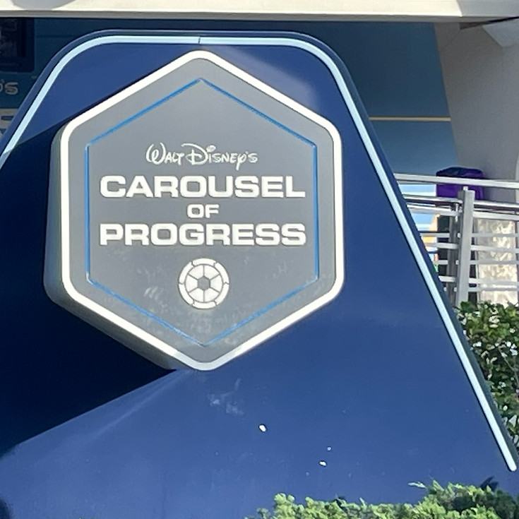 Entrance to Carousel of Progress at Magic Kingdom, with its rotating theater building and retro-futuristic sign inviting guests to experience the story of innovation through the decades.