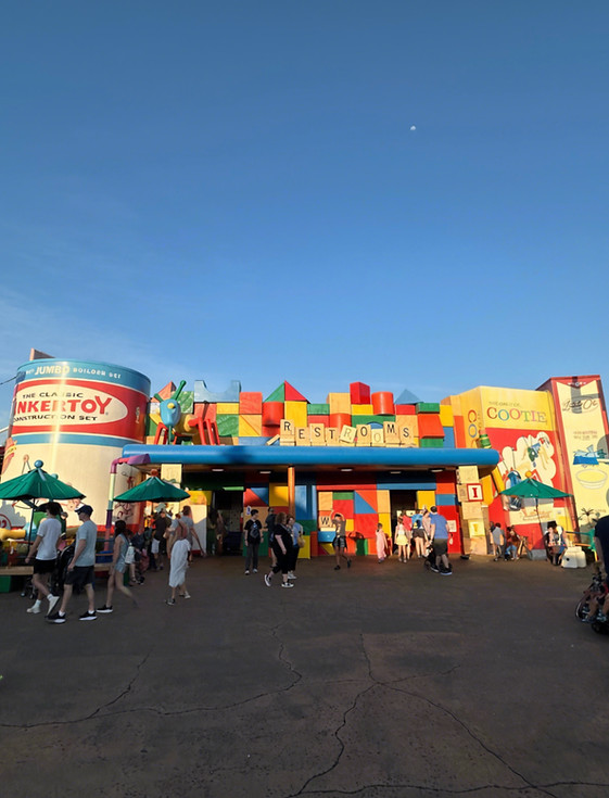 Brightly colored restroom sign in Toy Story Land with oversized toy blocks spelling out “Restrooms” beside a giant Cootie game box and Tinkeytoy box and playful decorations.