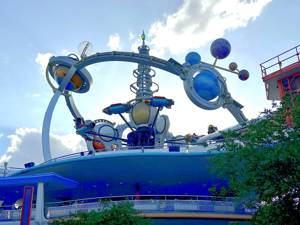 Close-up of Astro Orbiter at Magic Kingdom, showing the sleek metallic rockets spinning around a futuristic central tower with golden rings and planetary details against the sky.
