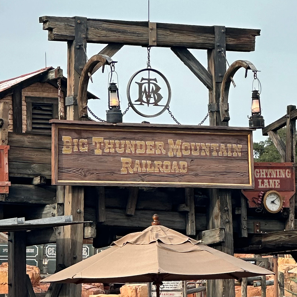 Big Thunder Mountain Railroad sign at Magic Kingdom, with rugged wooden planks and bold lettering, set against a backdrop of mining building and tools.