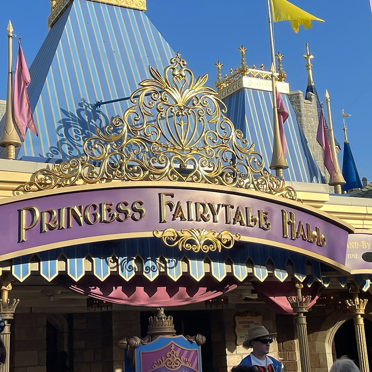 Princess Fairytale Hall sign at Magic Kingdom, featuring elegant gold script and royal crest details, set above the arched entryway to the regal princess meet and greet area.