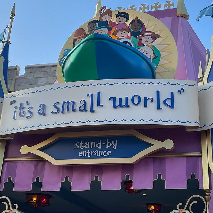 “it’s a small world” entrance sign at Magic Kingdom with colorful, playful lettering above the ride’s facade, and a boat above carrying cheerful character figures representing children from around the world.