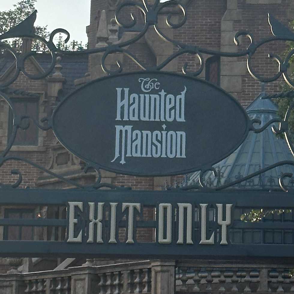 Haunted Mansion sign at Magic Kingdom, featuring an ornate, weathered plaque with gothic lettering mounted on a brick column, surrounded by eerie greenery and spooky atmosphere.