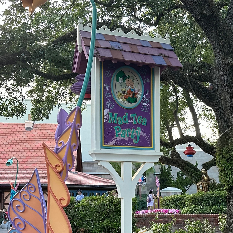 Mad Tea Party ride sign at Magic Kingdom, featuring colorful, swirling lettering and whimsical teacup designs, set near the open-air pavilion with spinning teacups under a festive canopy.