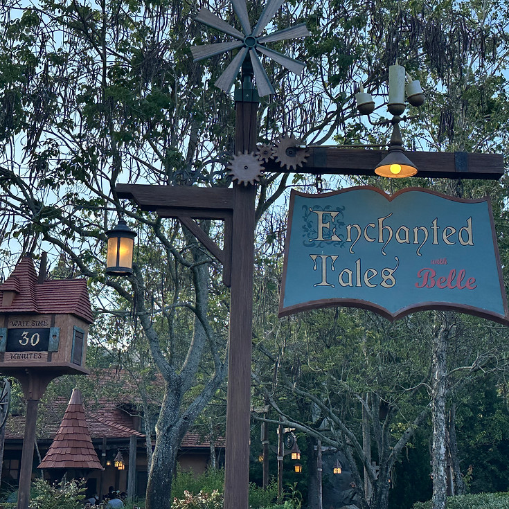 Enchanted Tales with Belle sign at Magic Kingdom, featuring storybook-style lettering with golden accents and magical flourishes near Maurice’s cottage.