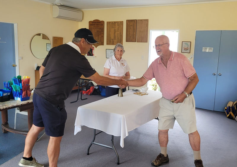 Two men shaking hands at a table, woman in background