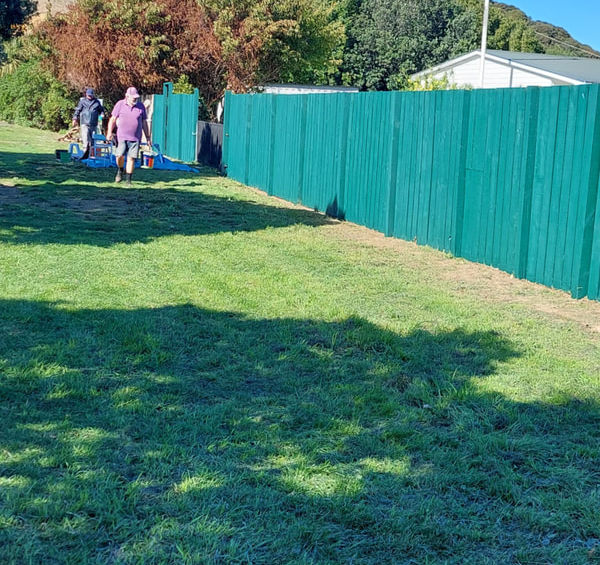 People walking beside a green fence on a grassy hill