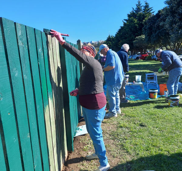 Volunteers painting a green wooden fence outdoors