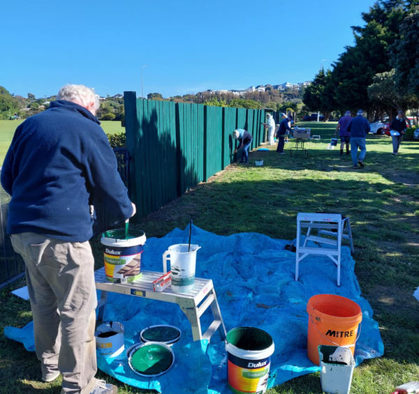 Volunteers painting a green fence outdoors