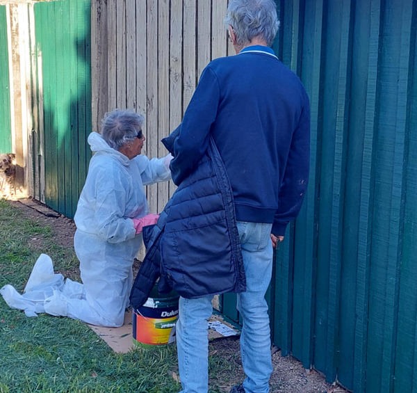 Two people painting a green fence