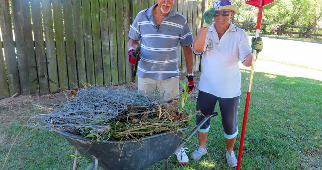 Two people with wheelbarrow full of garden waste and rake
