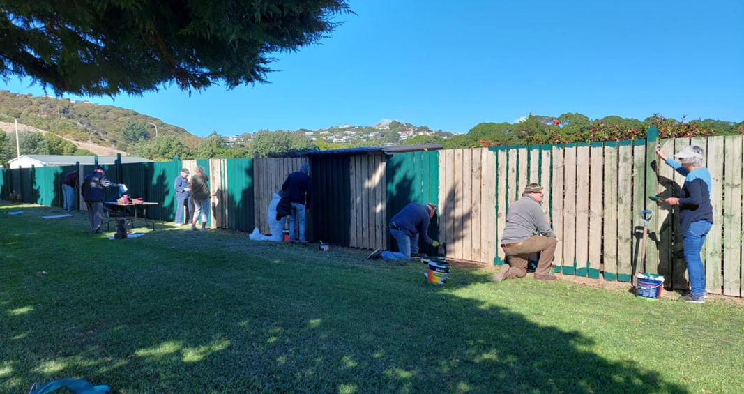 Group of people painting a wooden fence green outdoors