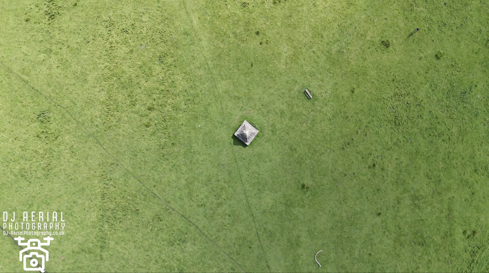 an aerial view of a green field with a pyramid in the middle