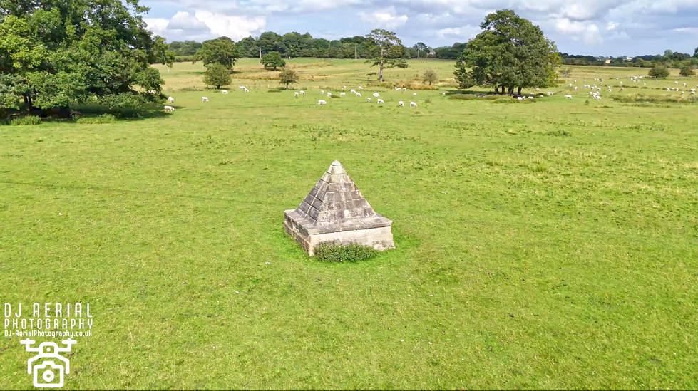 a stone pyramid in the middle of a grassy field