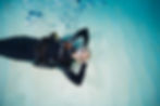 Scuba diver underwater, relaxed with hands behind head, bubbles rising in the water.