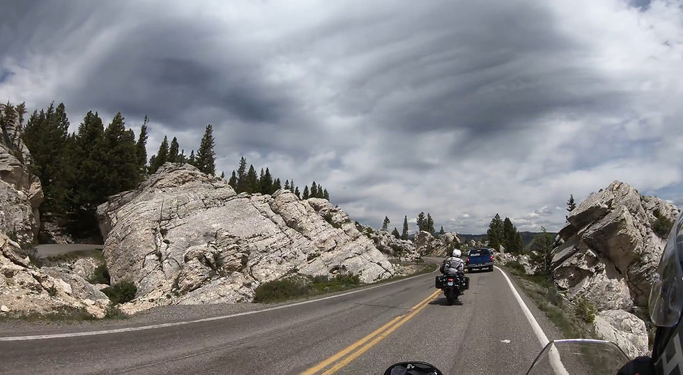View from a motorcycle on a road through red rock canyons. Clear blue sky, speedometer visible, "Suzuki" text on handlebar.