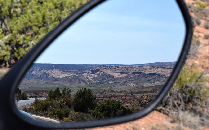A desert landscape viewed through the side mirror of a motorcycle