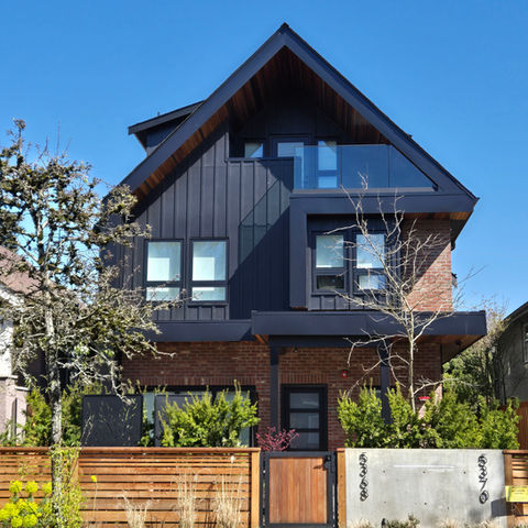 Front view of a front and back duplex with a main gable roof, brick and black board and batten cladding, and a fenced yard along Prince Edward Street.