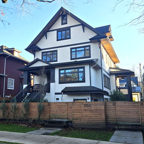Front view of a renovated character house converted to four strata homes, showing restored gable rooflines, new dormer, updated windows, and a fenced front yard.
