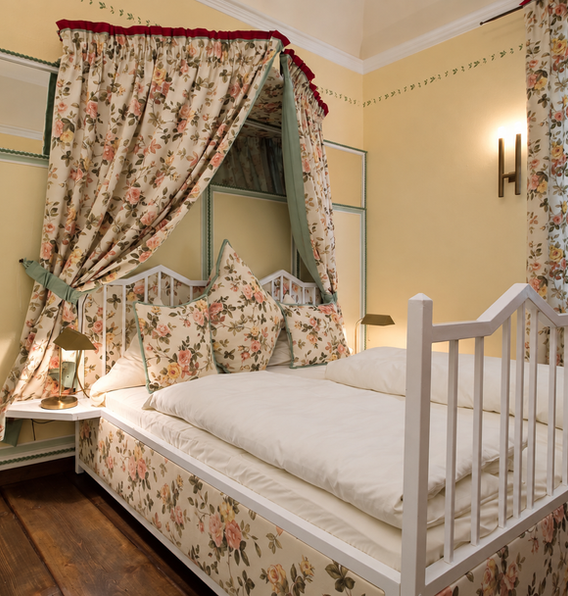 Schlosszimmer im ersten Stock mit hellem Himmelbett und gemusterten Stoffen