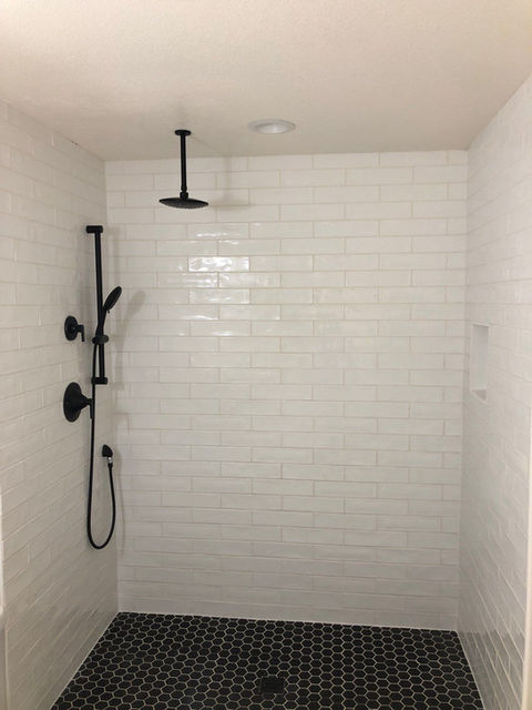 large white subway tiled shower with black hex tile floor and black hardware