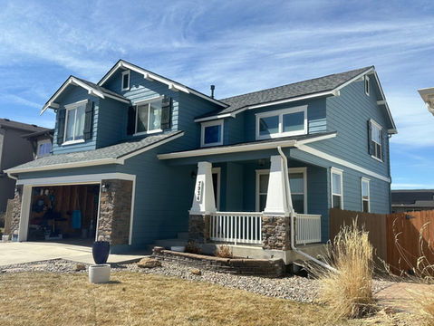 blue painted house with brown shutters, stone accents, and white pillars with cloudy blue sky background