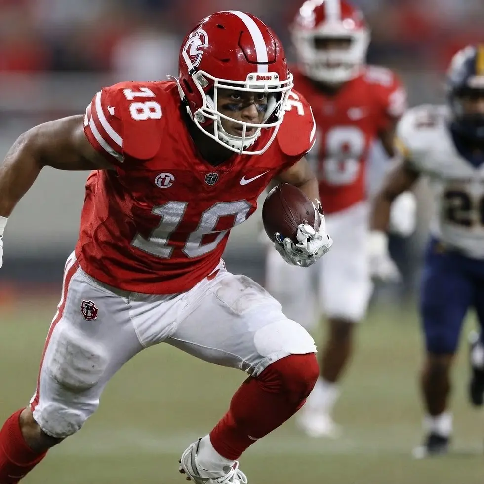 Sports photography depicting an American football player wearing a red jersey, number 18, sprinting with the ball. The scene is active and intense, set during a competition.