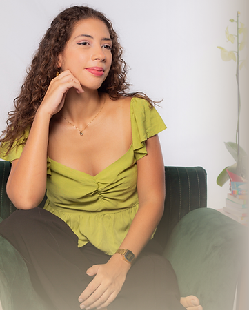 Foto de Rosa Paes sentada em uma poltrona verde, com o braço apoiando o queixo